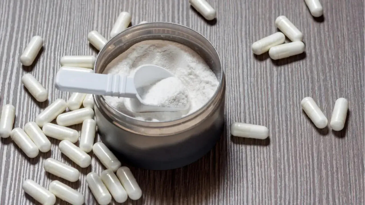 Cápsulas y polvo blanco sobre fondo de madera. Descubre para qué sirve la L-arginina y sus beneficios.