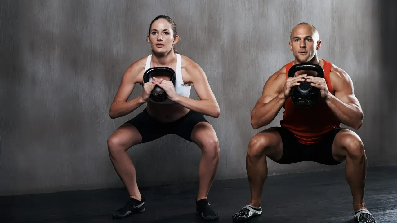 Hombre y mujer realizan sentadilla isométrica con kettlebell.