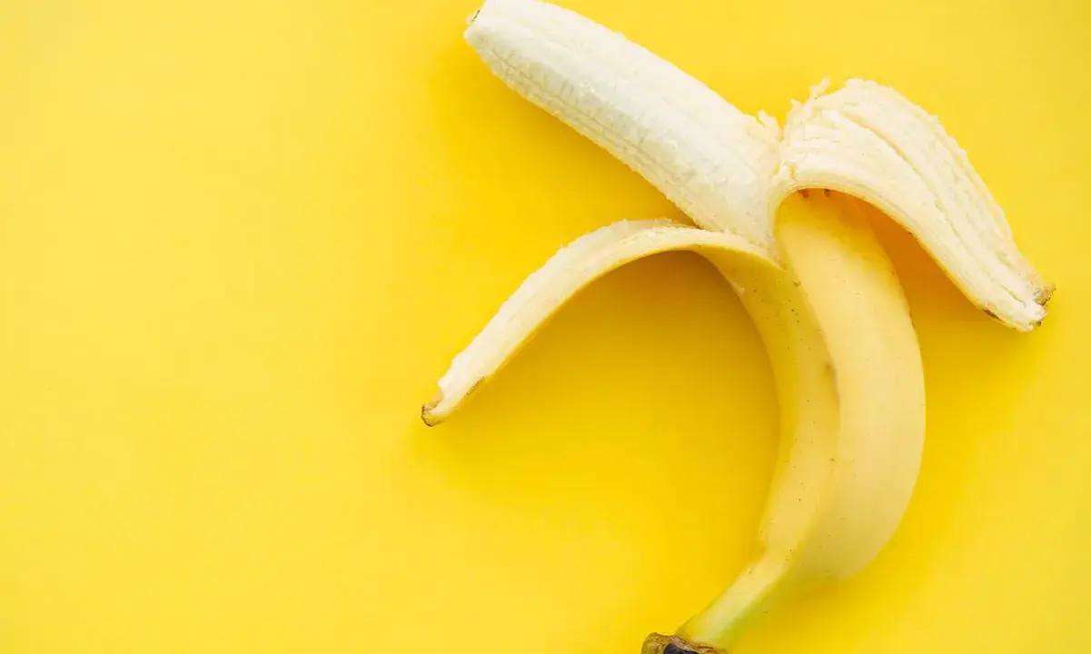 Plátano pelado sobre fondo amarillo. Un snack saludable con pocas calorías, ideal para deportistas.