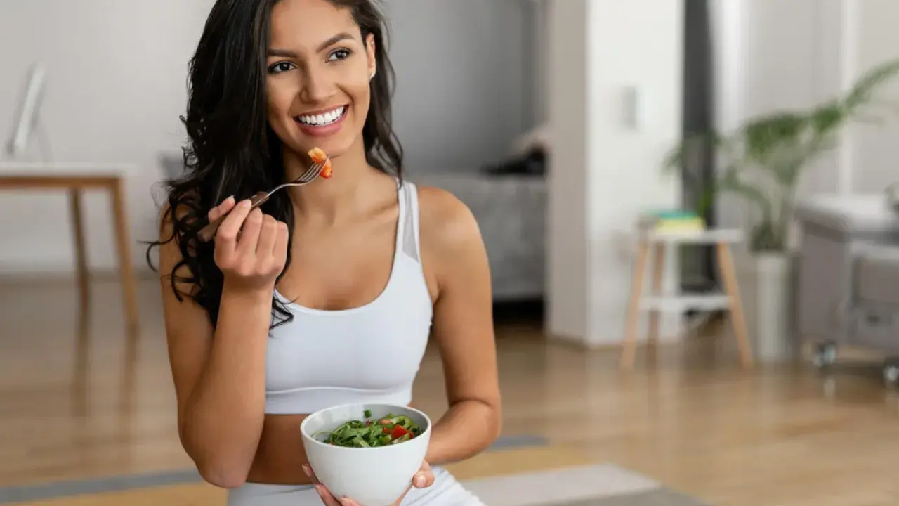 Mujer sonriente comiendo ensalada, equilibrando grelina y leptina para una vida saludable.