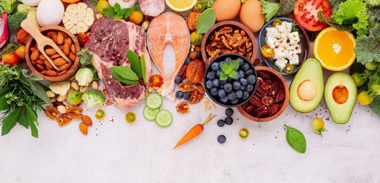 Ingredientes para un menú dieta keto: carne, salmón, huevos, aguacate, frutos secos, bayas, queso feta, verduras y hierbas frescas.