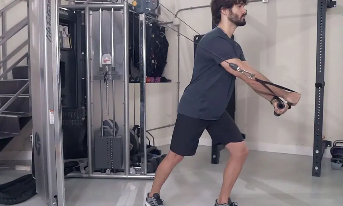 Hombre realizando ejercicio de cruce poleas en gimnasio.