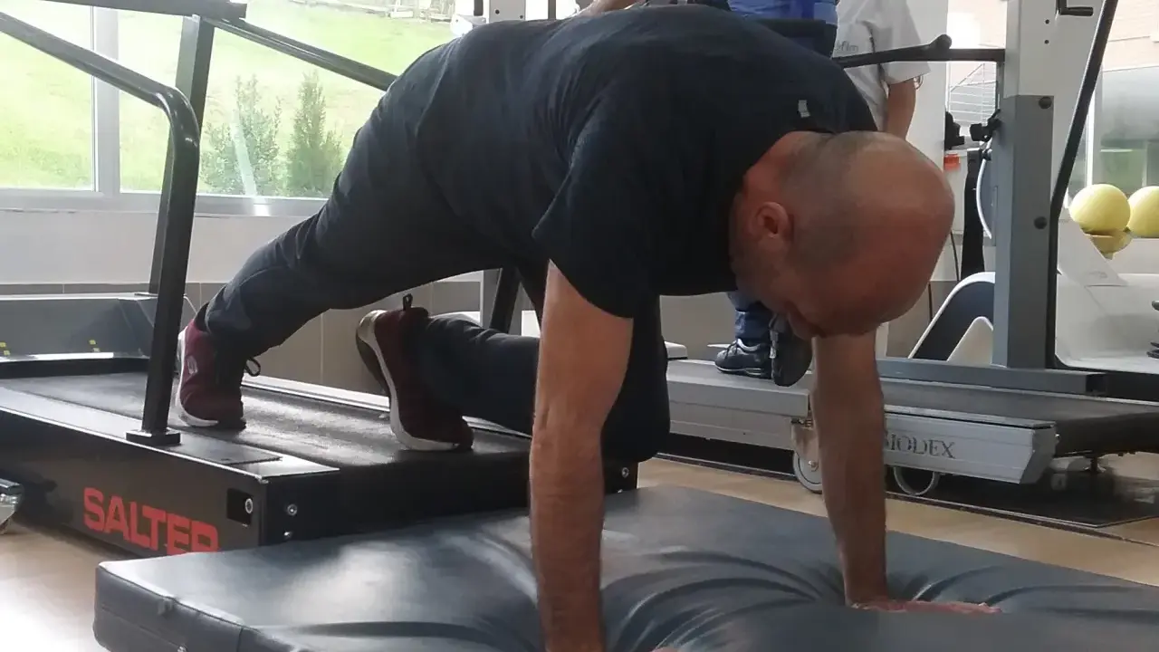 Hombre realizando ejercicio de cuadrupedia en una cinta de correr, con manos apoyadas en colchoneta.