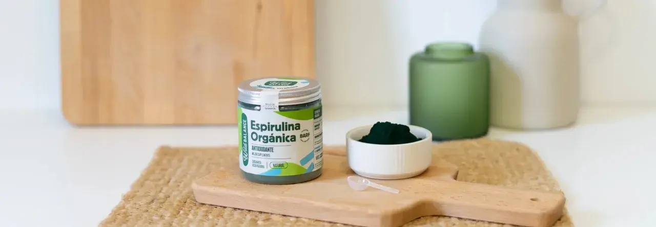 Un frasco de espirulina orgánica y una cucharita dosificadora sobre una tabla de madera. La espirulina es un superalimento antioxidante.