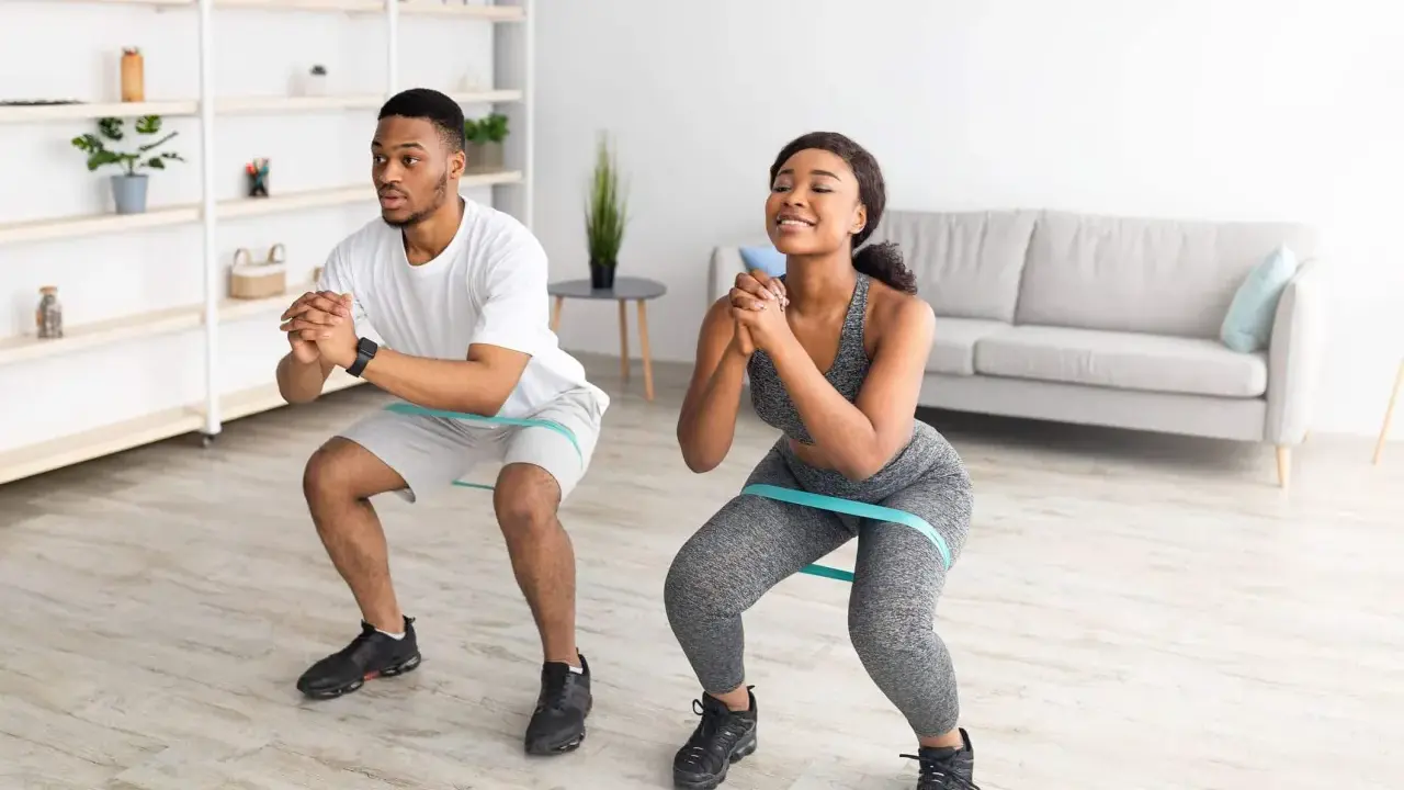 Pareja haciendo sentadillas con bandas elásticas para glúteos en casa.
