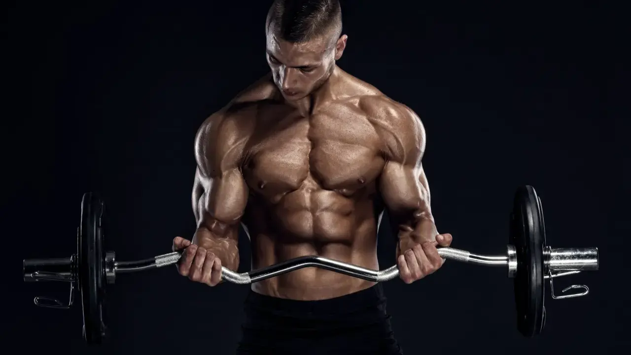 Hombre musculoso realizando curl en banco Scott con barra Z.