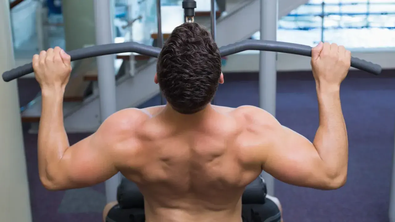 Hombre entrenando espalda con polea agarre cerrado. Músculos definidos trabajando en el gimnasio.
