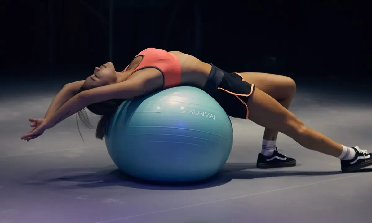 Mujer haciendo un curl femoral en fitball, estirando su espalda y brazos.