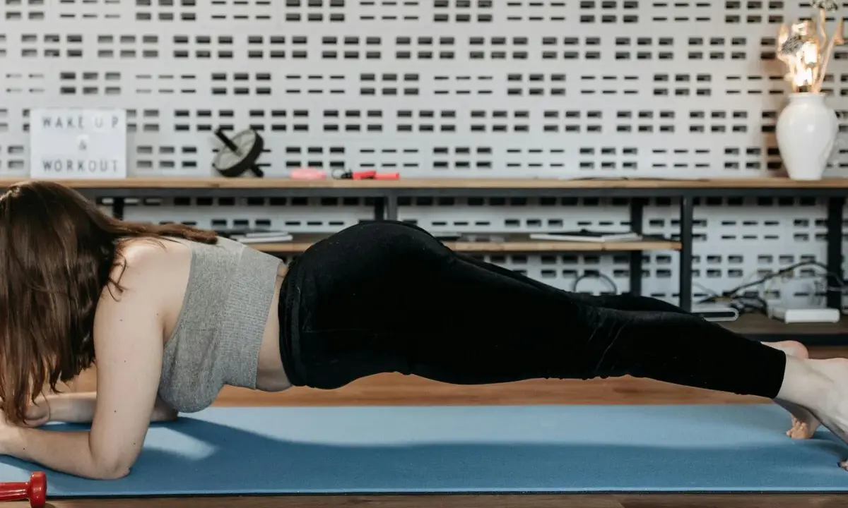 Mujer realizando ejercicio de **plancha antebrazos** en una esterilla azul.