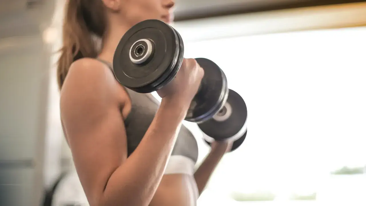 Mujer realizando ejercicio bíceps con mancuernas, enfocada en su entrenamiento.