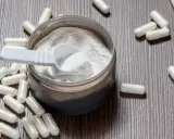 Cápsulas y polvo blanco sobre fondo de madera. Descubre para qué sirve la L-arginina y sus beneficios.