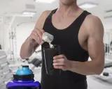 Hombre en gimnasio preparando batido con creatina para aumentar masa muscular.