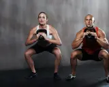 Hombre y mujer realizan sentadilla isométrica con kettlebell.