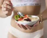 Mujer disfrutando un tazón de avena con fresas, kiwi y frutos secos. Un desayuno ideal para una dieta deficit calorico.