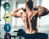 Hombre con espalda musculosa realizando un ejercicio de face pull sentado en el gimnasio.