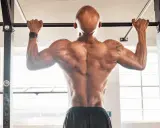 Hombre calvo haciendo dominadas, mostrando su espalda musculosa. Parte de su rutina de espalda gym.