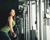 Mujer asiática realiza extensión de triceps en maquina de poleas, concentrada en su entrenamiento.