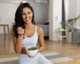 Mujer sonriente comiendo ensalada, equilibrando grelina y leptina para una vida saludable.