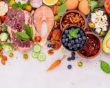 Ingredientes para un menú dieta keto: carne, salmón, huevos, aguacate, frutos secos, bayas, queso feta, verduras y hierbas frescas.