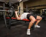 Hombre haciendo press banca con barra en un gimnasio.