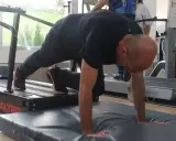 Hombre realizando ejercicio de cuadrupedia en una cinta de correr, con manos apoyadas en colchoneta.