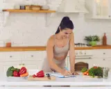 Mujer sonriente planifica su dieta vegetariana para deportistas en la cocina, rodeada de verduras frescas.