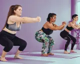 Tres mujeres realizan sentadilla con apoyo en un estudio de yoga.