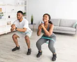Pareja haciendo sentadillas con bandas elásticas para glúteos en casa.