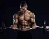 Hombre musculoso realizando curl en banco Scott con barra Z.