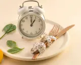 Reloj, plato, cubiertos con cinta métrica y hojas verdes. Símbolos de los beneficios del ayuno intermitente y un estilo de vida saludable.