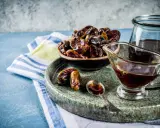 Un tazón de dátiles secos y un jarabe oscuro en una salsera, listos para endulzar con dátiles de forma natural.