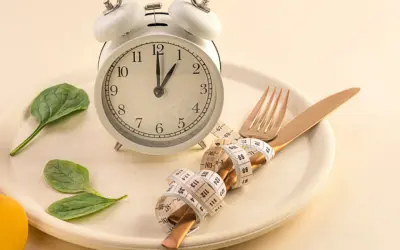 Reloj, plato, cubiertos con cinta métrica y hojas verdes. Símbolos de los beneficios del ayuno intermitente y un estilo de vida saludable.