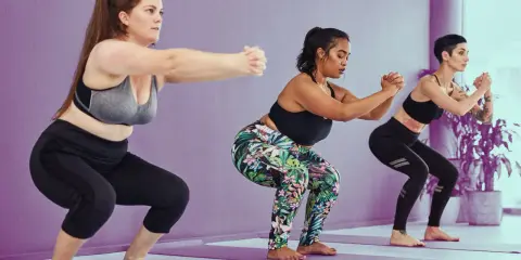 Tres mujeres realizan sentadilla con apoyo en un estudio de yoga.