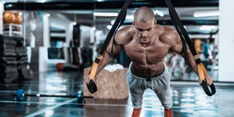 Hombre musculoso realizando trx ejercicios en un gimnasio, con el cuerpo tenso y sudoroso.