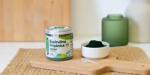 Un frasco de espirulina orgánica y una cucharita dosificadora sobre una tabla de madera. La espirulina es un superalimento antioxidante.