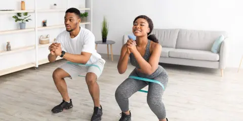 Pareja haciendo sentadillas con bandas elásticas para glúteos en casa.