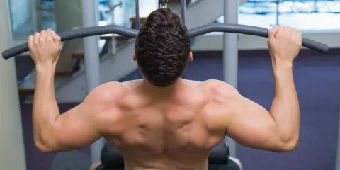 Hombre entrenando espalda con polea agarre cerrado. Músculos definidos trabajando en el gimnasio.