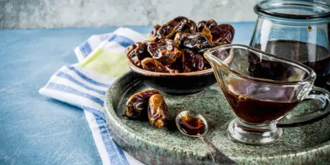 Un tazón de dátiles secos y un jarabe oscuro en una salsera, listos para endulzar con dátiles de forma natural.