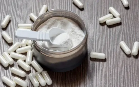 Cápsulas y polvo blanco sobre fondo de madera. Descubre para qué sirve la L-arginina y sus beneficios.