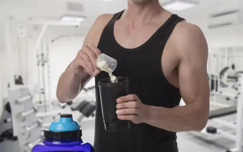 Hombre en gimnasio preparando batido con creatina para aumentar masa muscular.