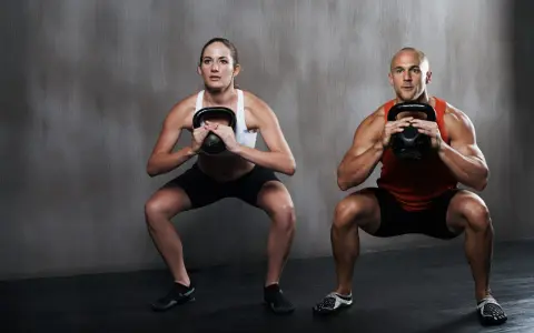 Hombre y mujer realizan sentadilla isométrica con kettlebell.