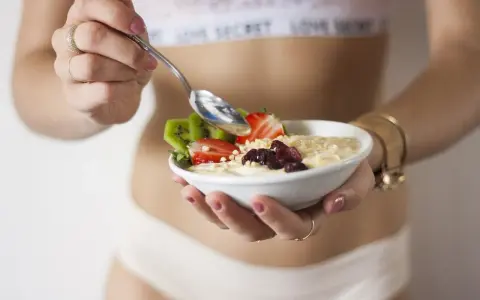 Mujer disfrutando un tazón de avena con fresas, kiwi y frutos secos. Un desayuno ideal para una dieta deficit calorico.