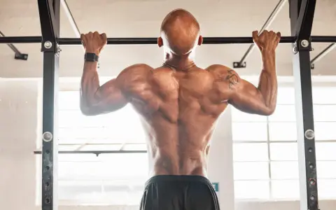 Hombre calvo haciendo dominadas, mostrando su espalda musculosa. Parte de su rutina de espalda gym.