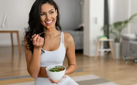 Mujer sonriente comiendo ensalada, equilibrando grelina y leptina para una vida saludable.