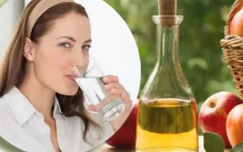 Mujer bebe agua, junto a botella de vinagre de manzana y manzanas. Una rutina saludable para tomar vinagre de manzana en ayunas.