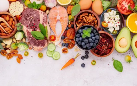 Ingredientes para un menú dieta keto: carne, salmón, huevos, aguacate, frutos secos, bayas, queso feta, verduras y hierbas frescas.