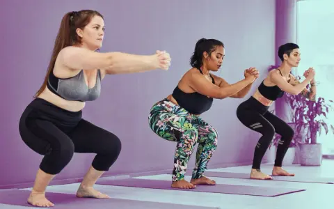 Tres mujeres realizan sentadilla con apoyo en un estudio de yoga.