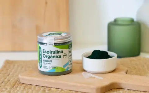 Un frasco de espirulina orgánica y una cucharita dosificadora sobre una tabla de madera. La espirulina es un superalimento antioxidante.