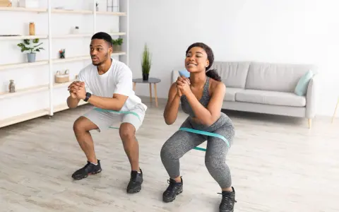 Pareja haciendo sentadillas con bandas elásticas para glúteos en casa.