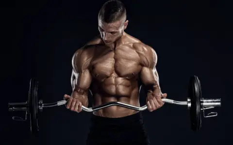 Hombre musculoso realizando curl en banco Scott con barra Z.
